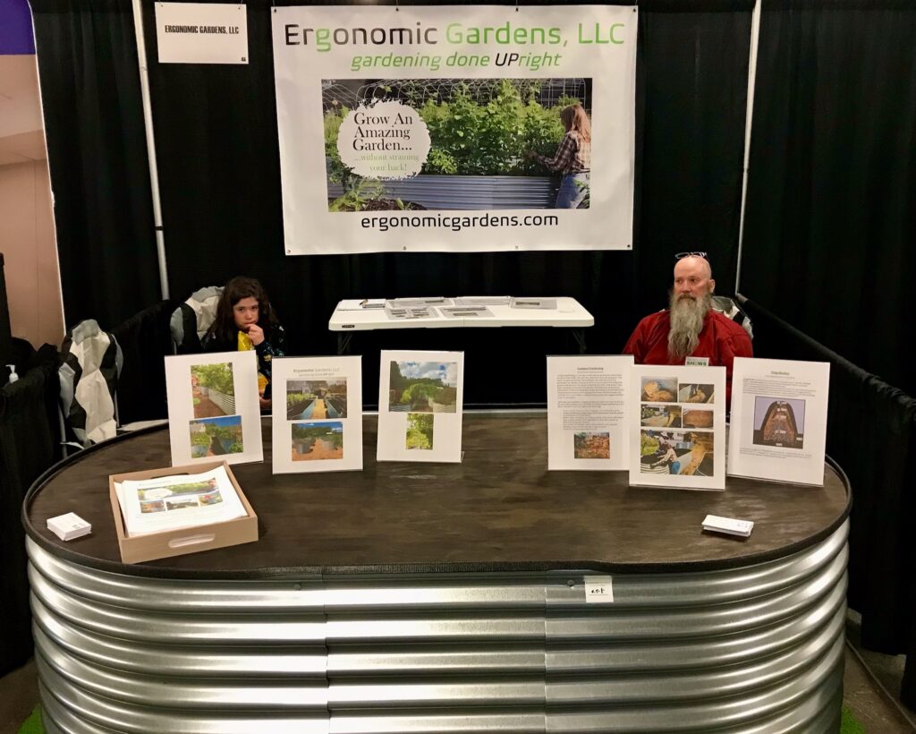 Founder, Chris with large, elevated planter or raised garden bed (Evolution Garden) at Home and Food Truck Show at Topsfield Fairgrounds, Massachusetts. Booth also contains Ergonomic Gardens, LLC banner and display materials.